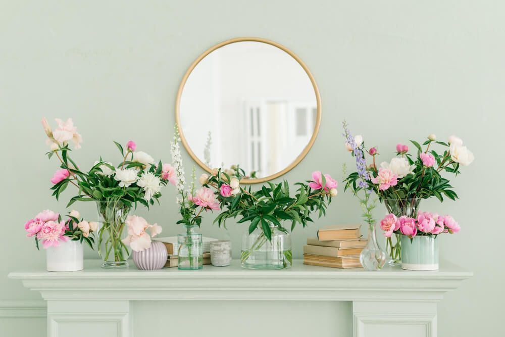 Pivoines roses et blanches dans des vases en verre sur l'étagère. Miroir rond et doré au-dessus de la cheminée