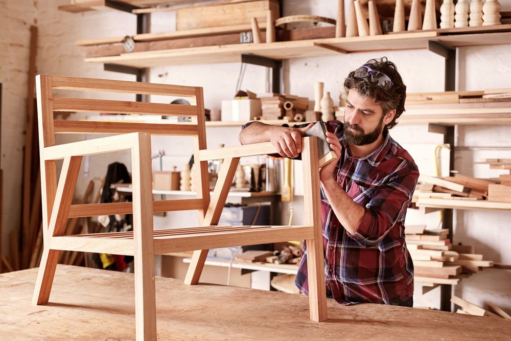 man sanding a wooden chair with a block