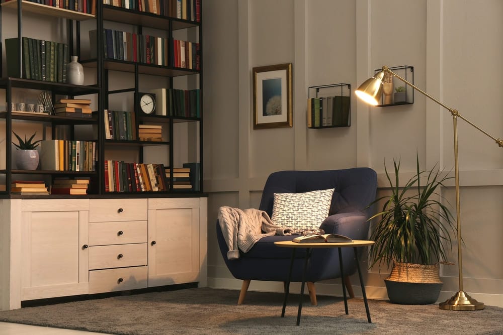 Escritório com luminária para leitura, poltrona azul, plantas e uma estante de livros